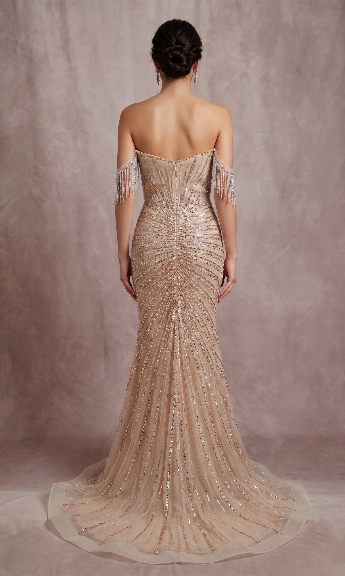 A woman faces away from the camera wearing the Chicas C847 Long Formal Dress—a blush, off-the-shoulder embellished sheath gown with intricate beadwork and fringe sleeve details, set against a neutral backdrop.